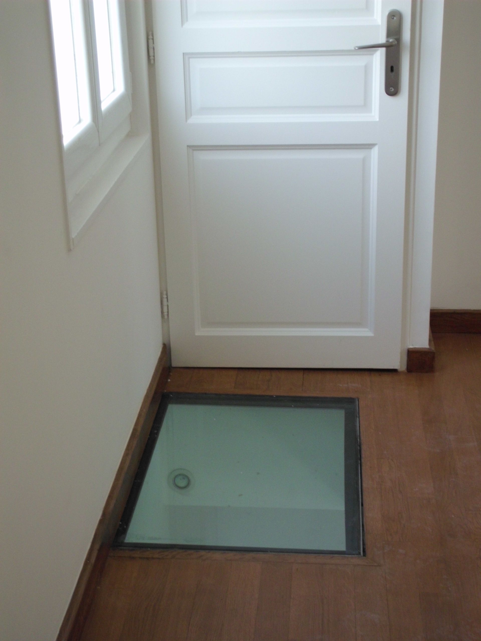 Petite dalle de sol en verre près d'une porte blanche.