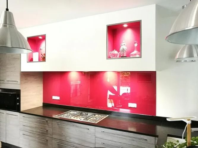 Cuisine moderne avec placards gris, plan de travail noir, crédence en verre rouge et étagères encastrées avec objets décoratifs.