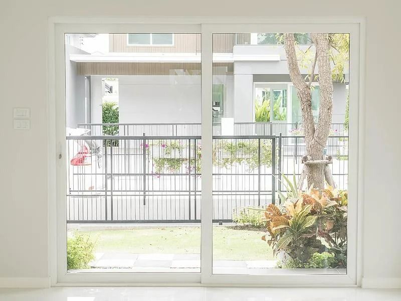Porte-fenêtre coulissante donnant sur un jardin arrière avec un arbre, un jardin, une clôture et des maisons en arrière-plan.