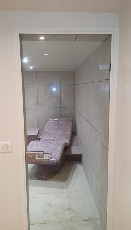 Une petite cabine de spa avec un siège inclinable, des murs carrelés et une porte vitrée.