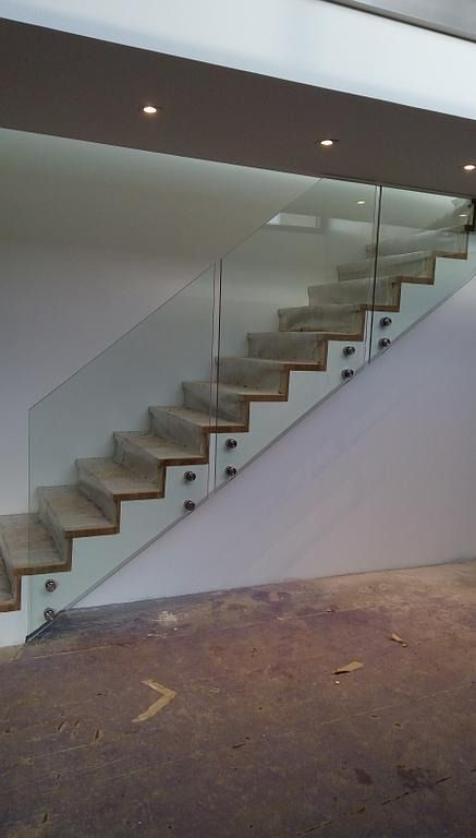 Escalier avec marches en bois et rambarde en verre fixé à un mur blanc.