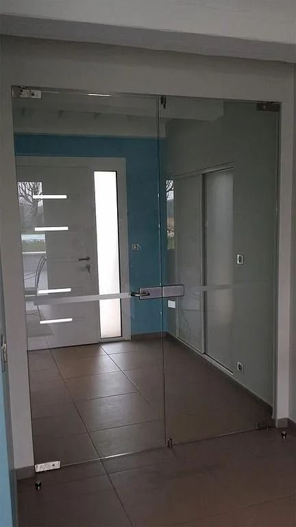 Des doubles portes vitrées transparentes donnent sur une pièce avec une porte blanche et un mur bleu.