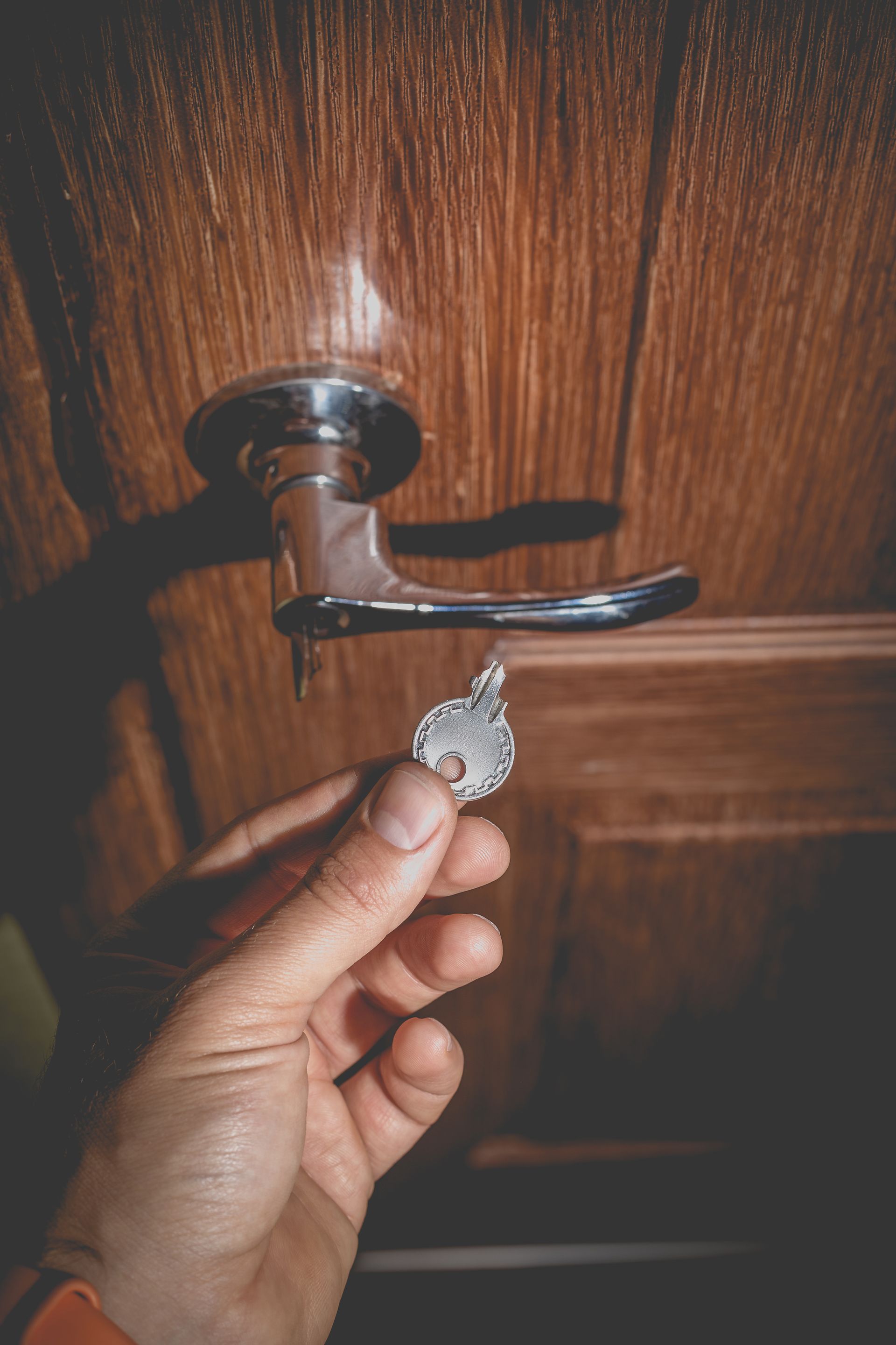 Main qui tien une clé cassé face à une porte en bois