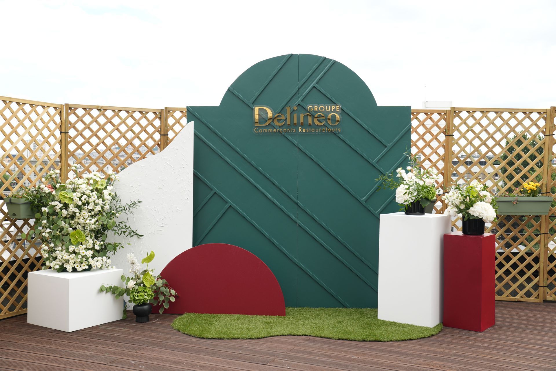 Décor extérieur avec panneau vert, clôture en treillis, jardinières blanches et touches de rouge sur pavé de briques.