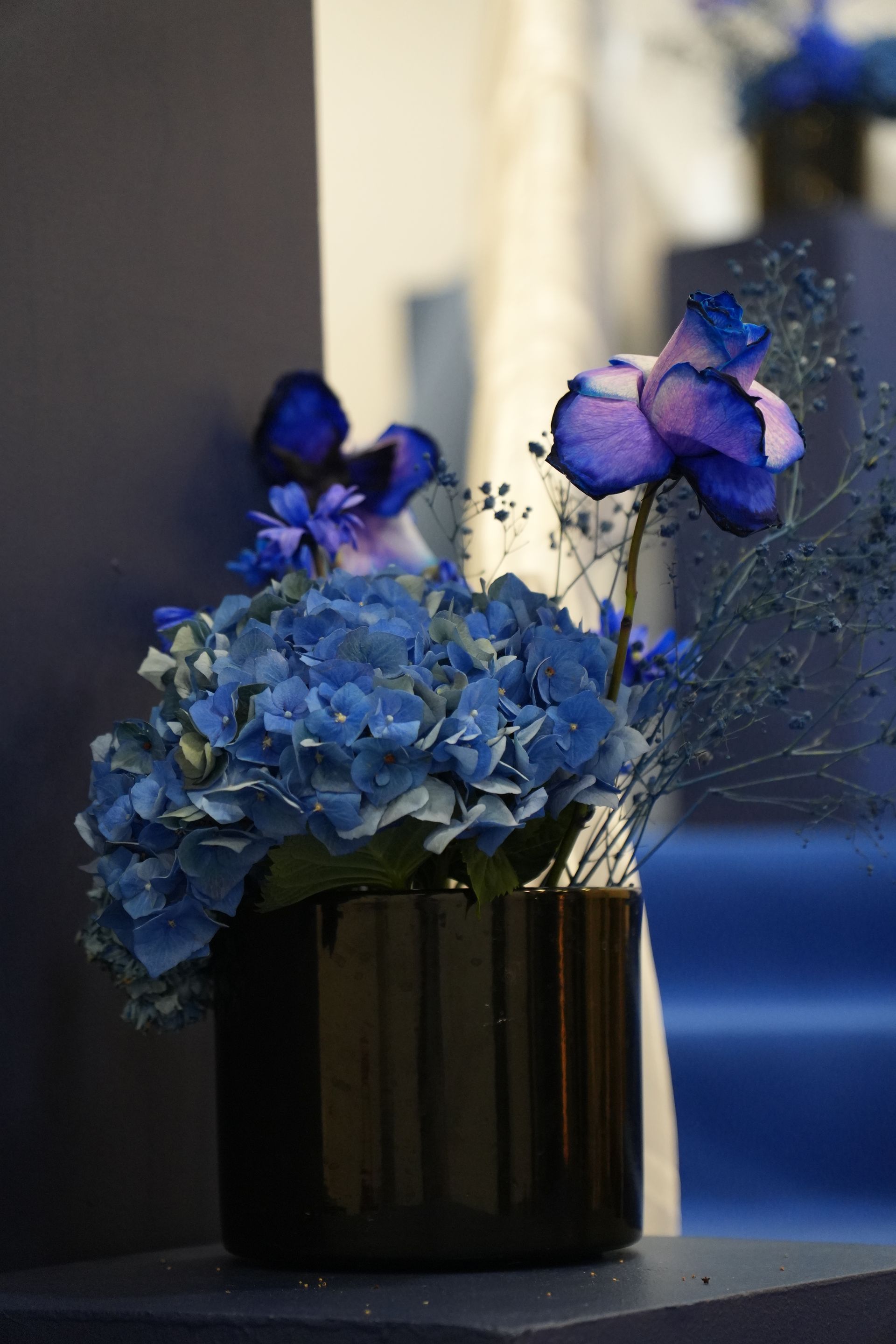 Des fleurs bleues et violettes disposées dans un vase sombre sur une table