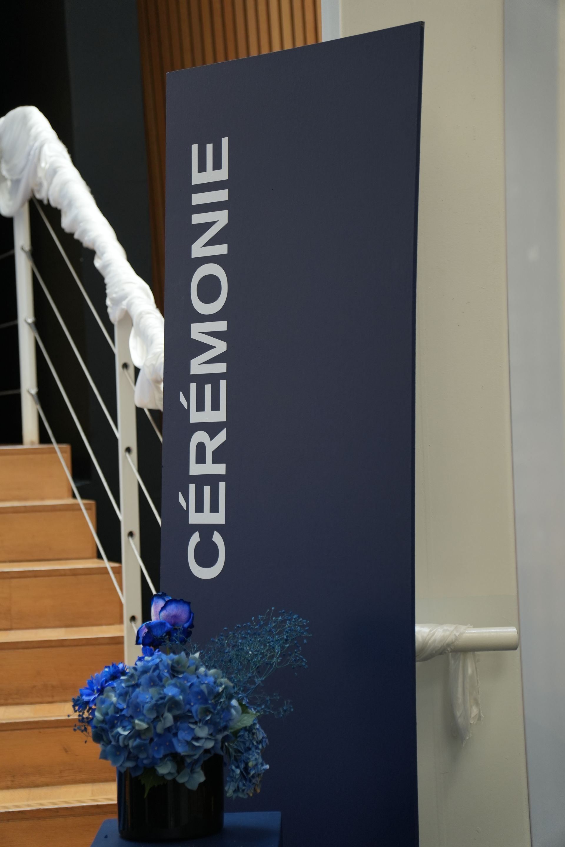 Bannière CEREMONIE à côté d'un escalier, avec un arrangement floral bleu au premier plan.