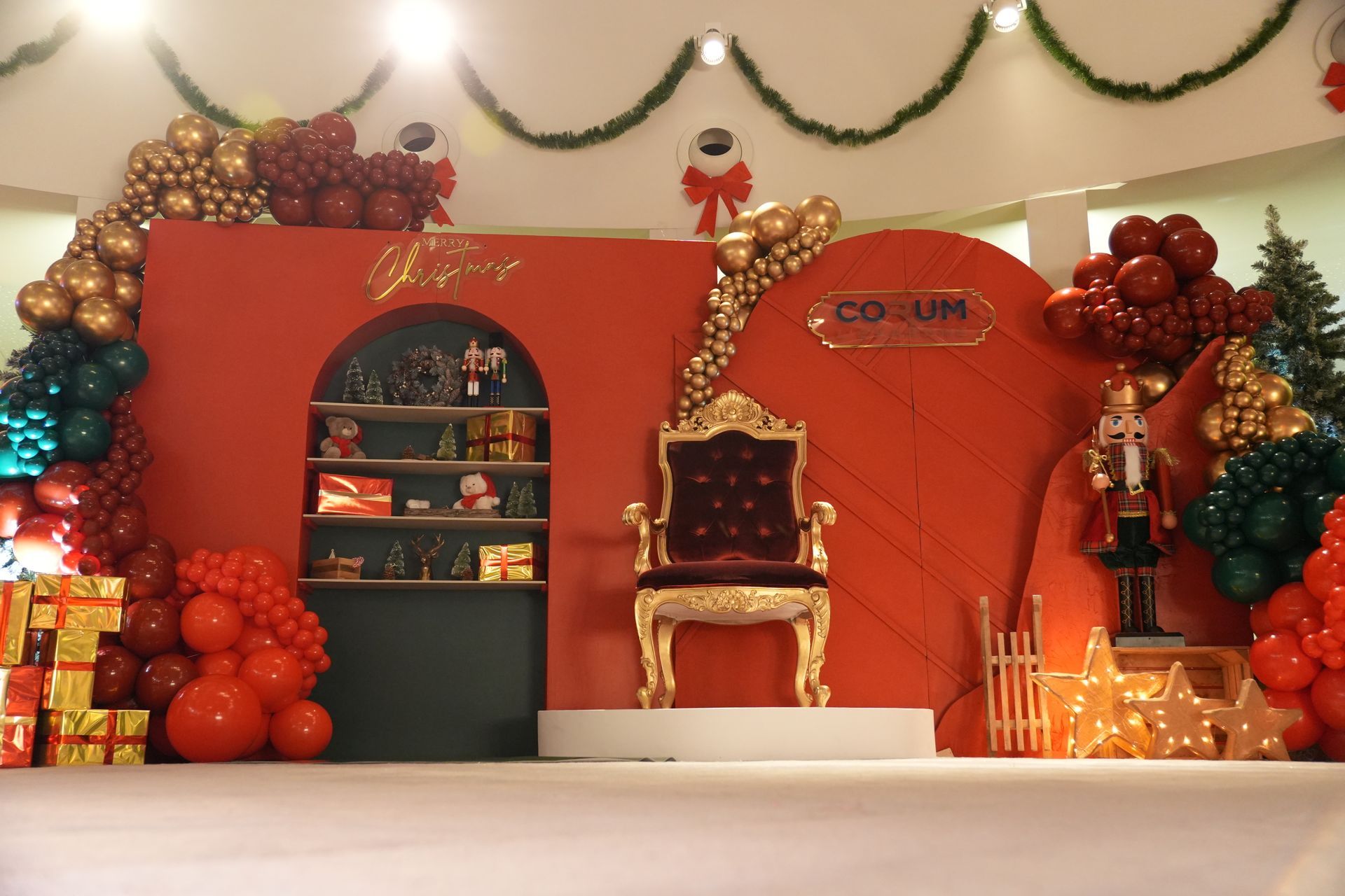Scène festive rouge et or avec un trône décoré, des étagères en forme d'arche et des guirlandes.
