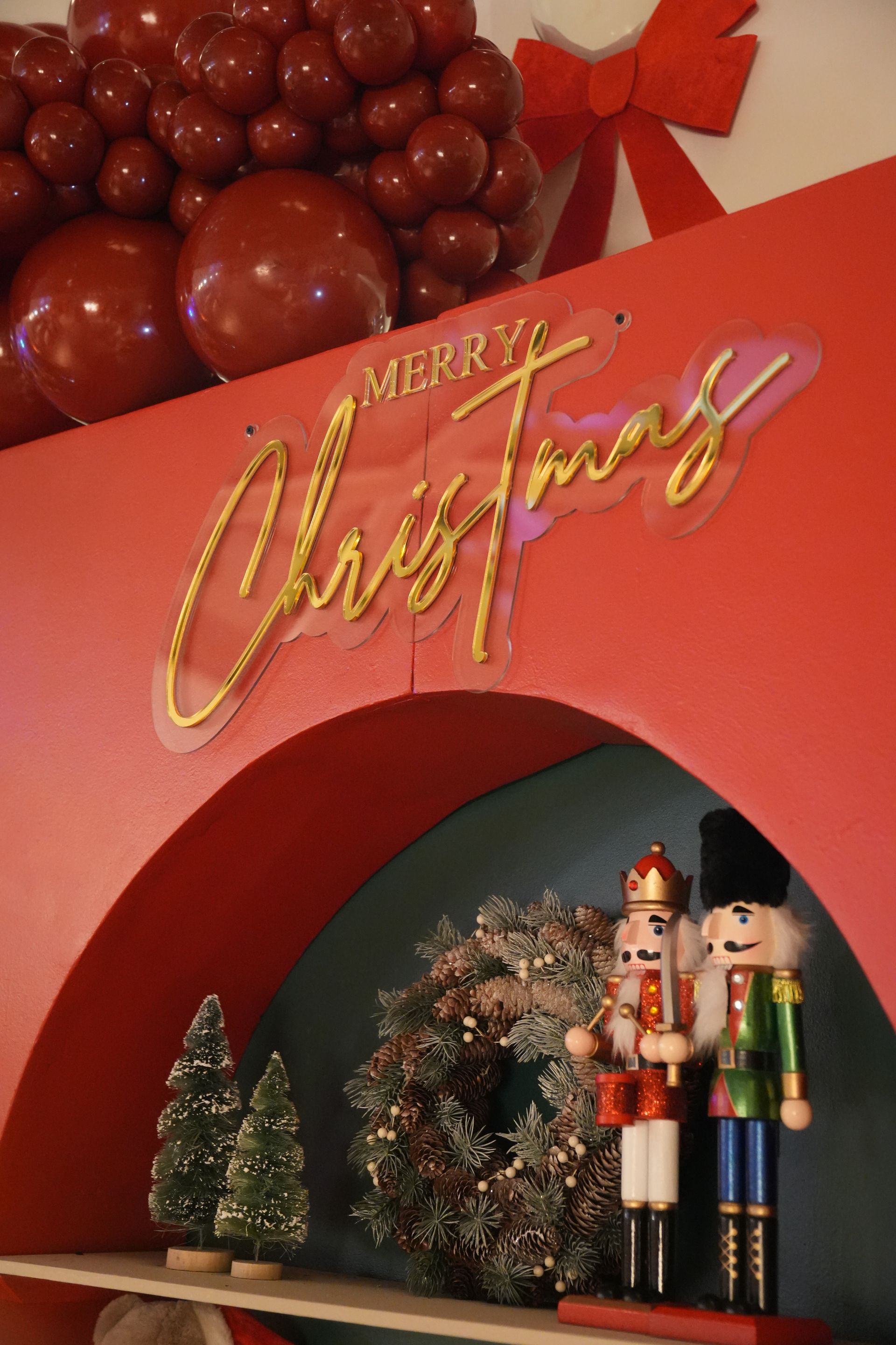 Décoration de Noël avec des ballons rouges, une pancarte dorée « Joyeux Noël » et des figurines festives sous une arche