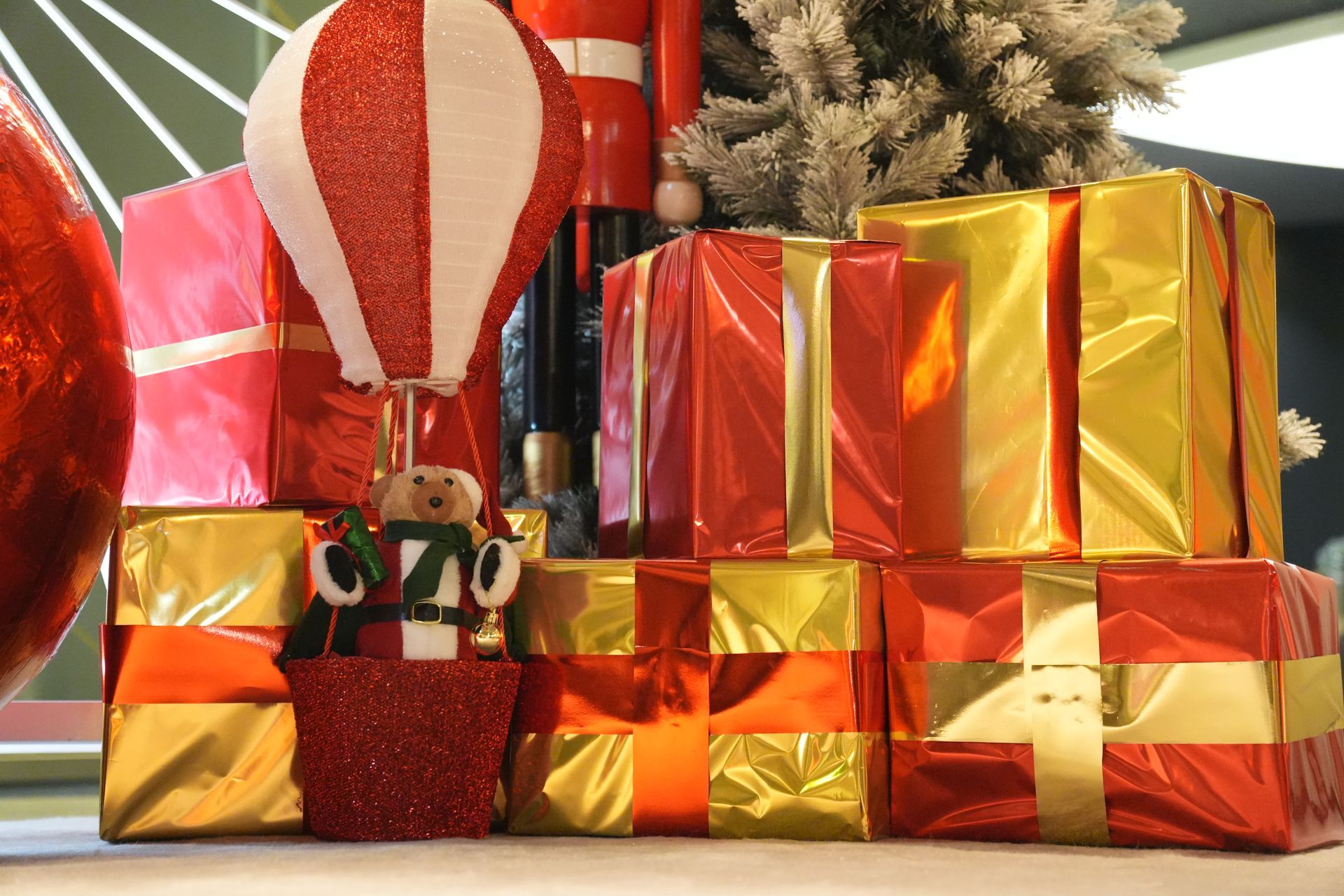 Des cadeaux de Noël emballés dans du papier rouge et doré sont empilés à côté d'une décoration de Père Noël et d'un petit sapin.