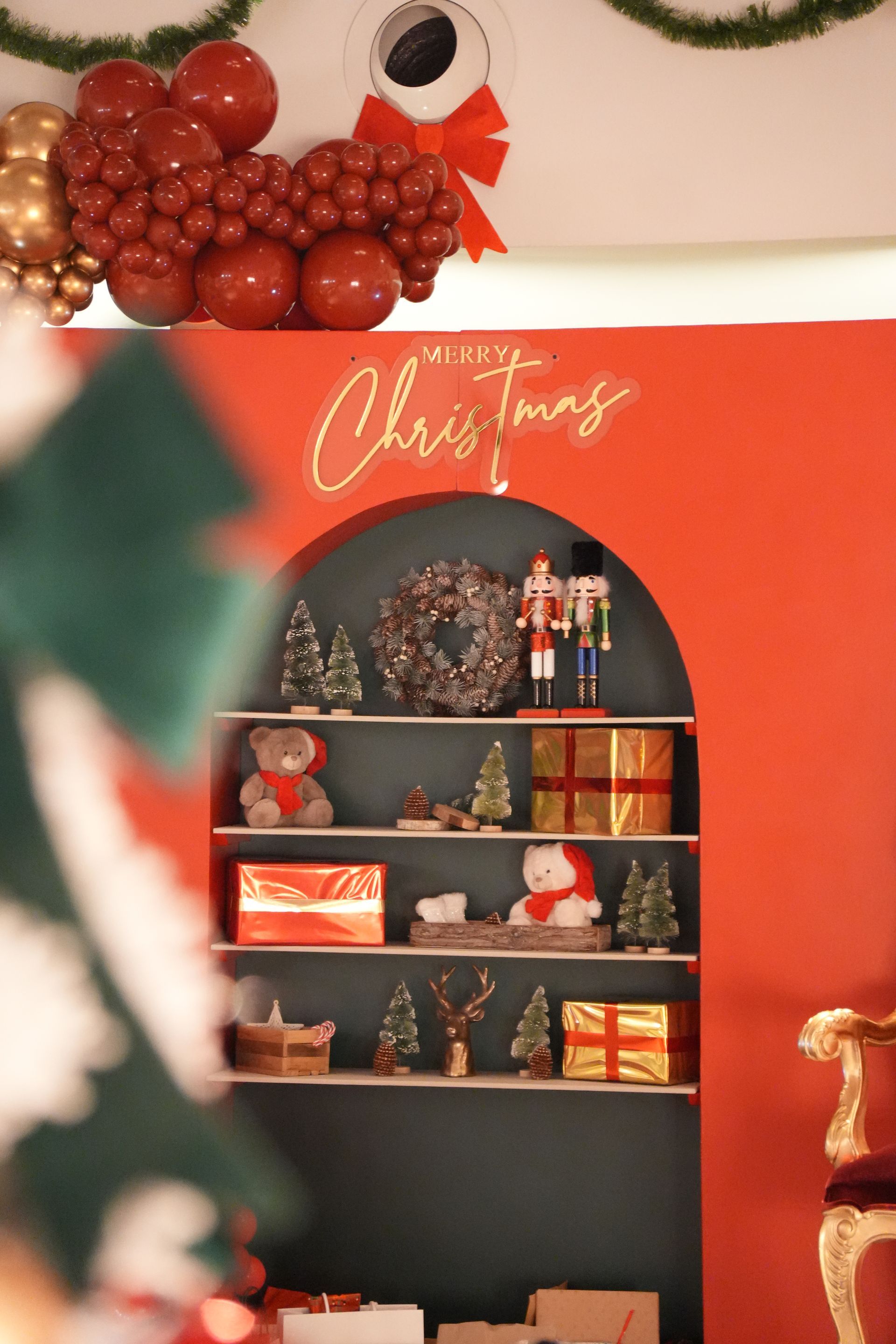 Étagère de Noël avec décorations, cadeaux emballés et ornements rouges sur un mur rouge