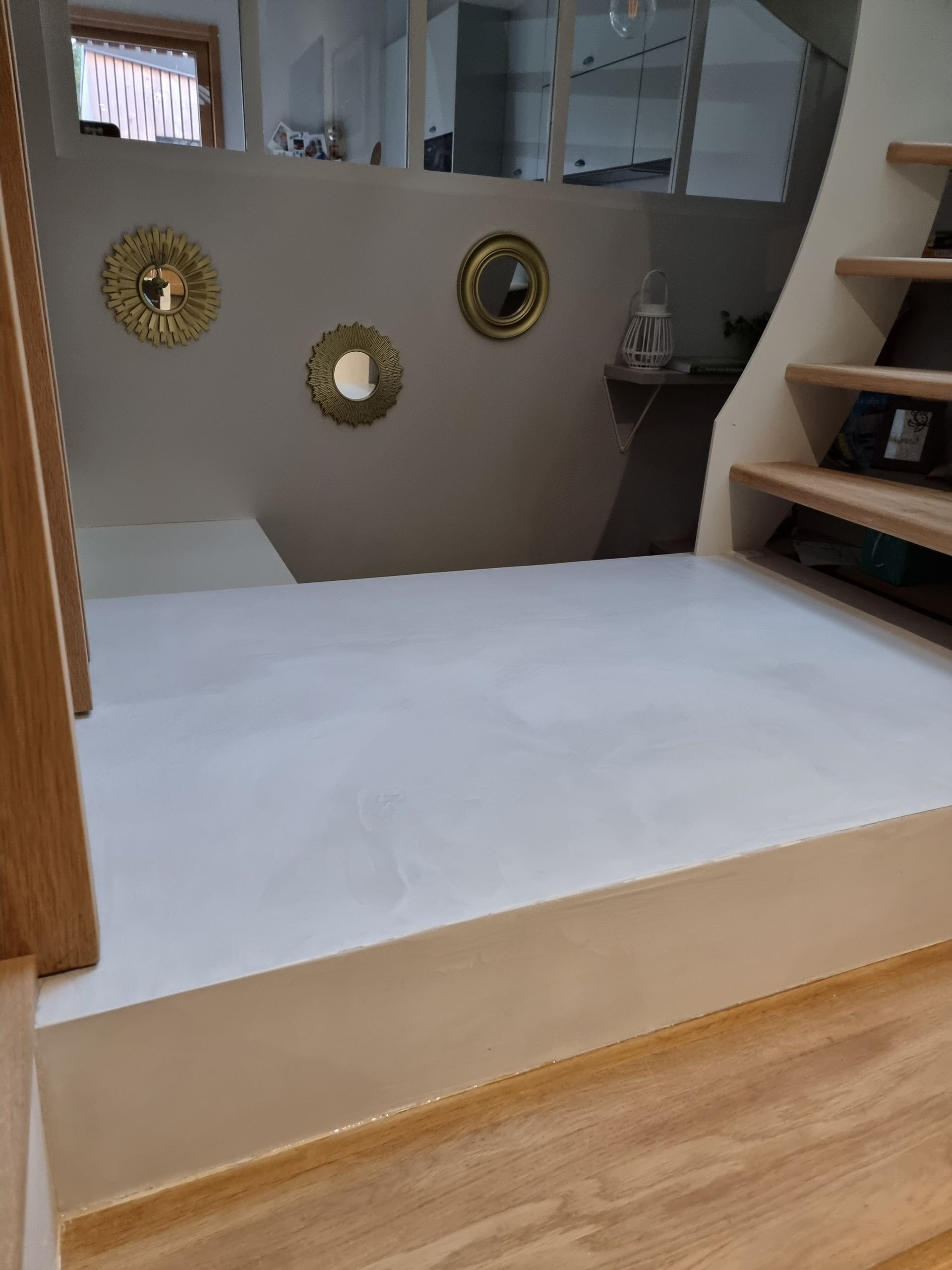 Un palier d'escalier clair jouxte un escalier en bois, orné d'un mur décoré de trois miroirs circulaires à bordure dorée.