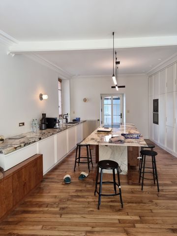 Une cuisine moderne et minimaliste avec des armoires blanches, des comptoirs en marbre, un îlot central et un parquet.