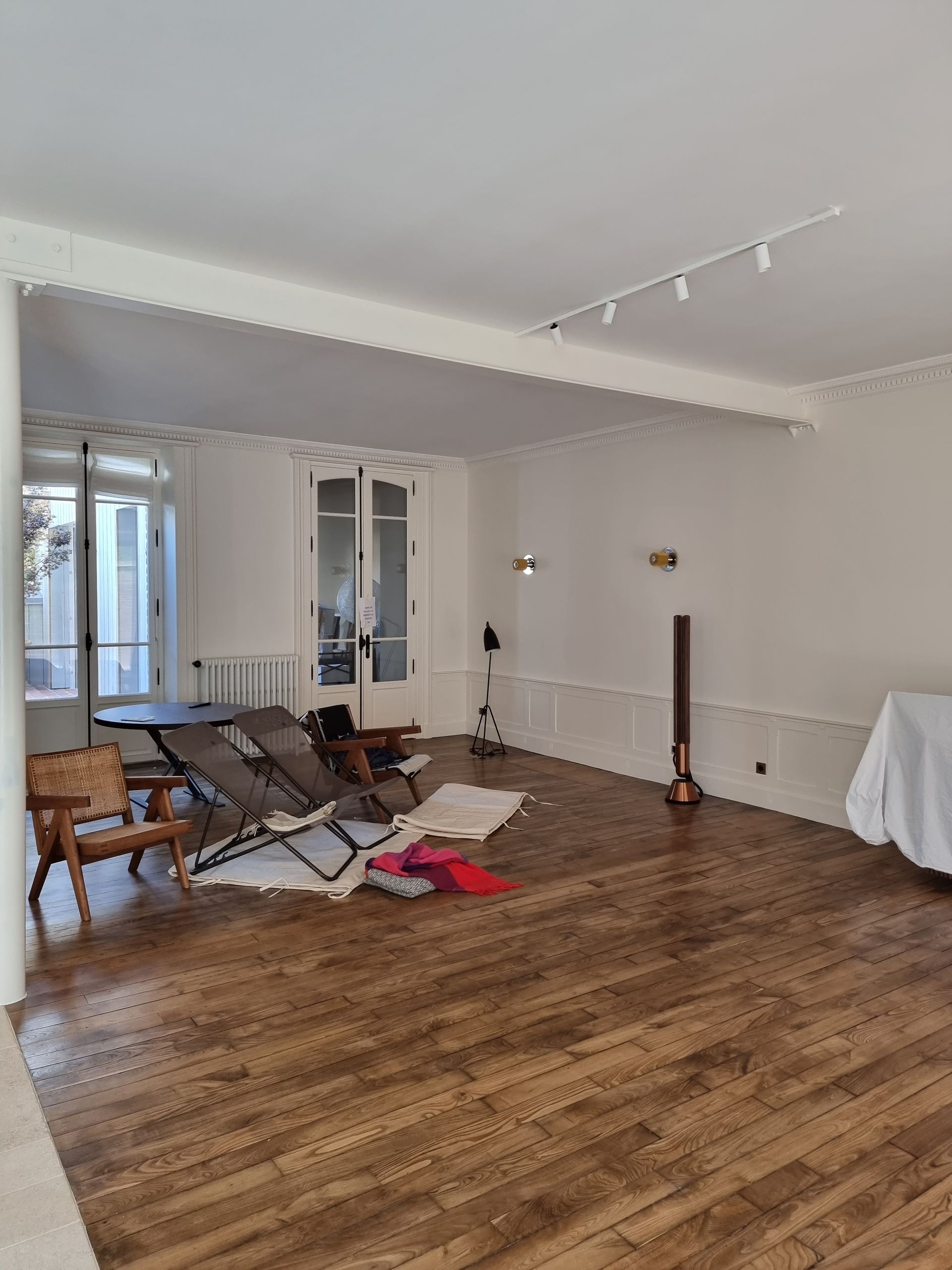 Une pièce lumineuse avec parquet, comprenant un coin salon décontracté avec des chaises pliantes et un meuble recouvert.