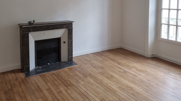 Une pièce vide avec un parquet clair, des murs blancs et une cheminée décorative en marbre foncé.