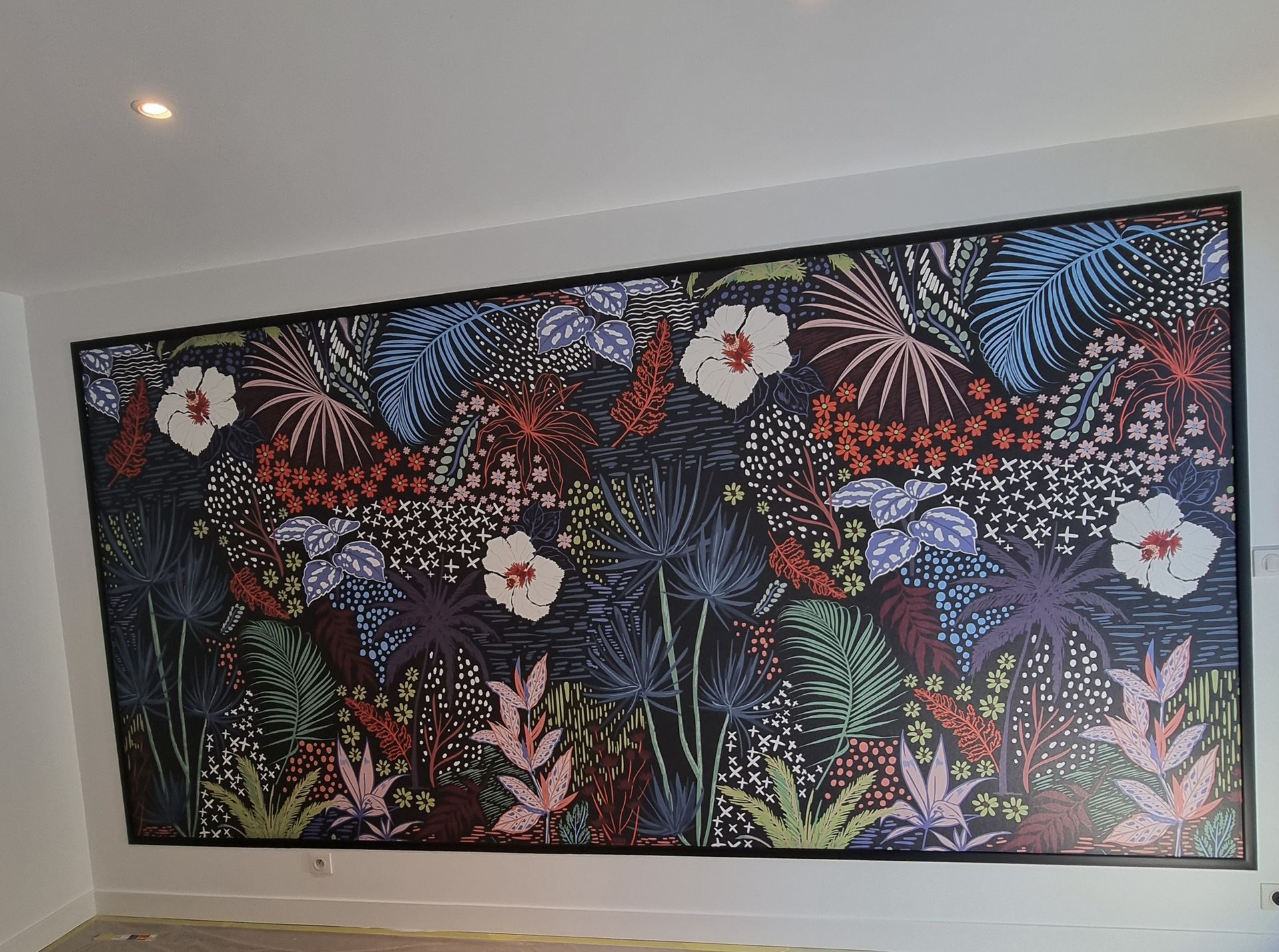 Une grande fresque murale rectangulaire présentant un motif tropical dense et coloré avec des fleurs d'hibiscus blanches sur un fond sombre.