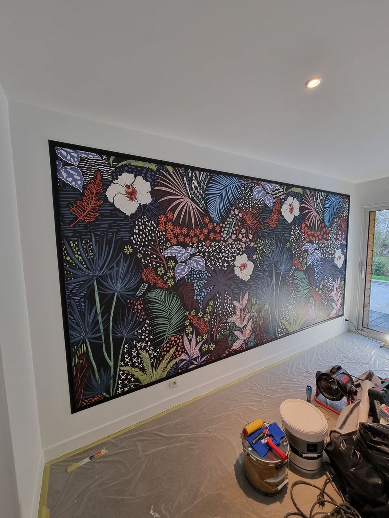 Une grande fresque murale en papier peint à motifs floraux colorés sur un mur blanc dans une pièce en cours de rénovation.