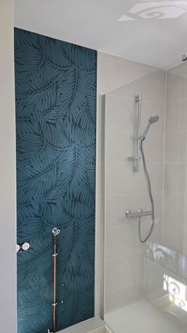 Une douche de salle de bains avec un mur d'accent bleu foncé texturé à motifs de feuilles, à côté d'une douche vitrée avec des accessoires argentés.