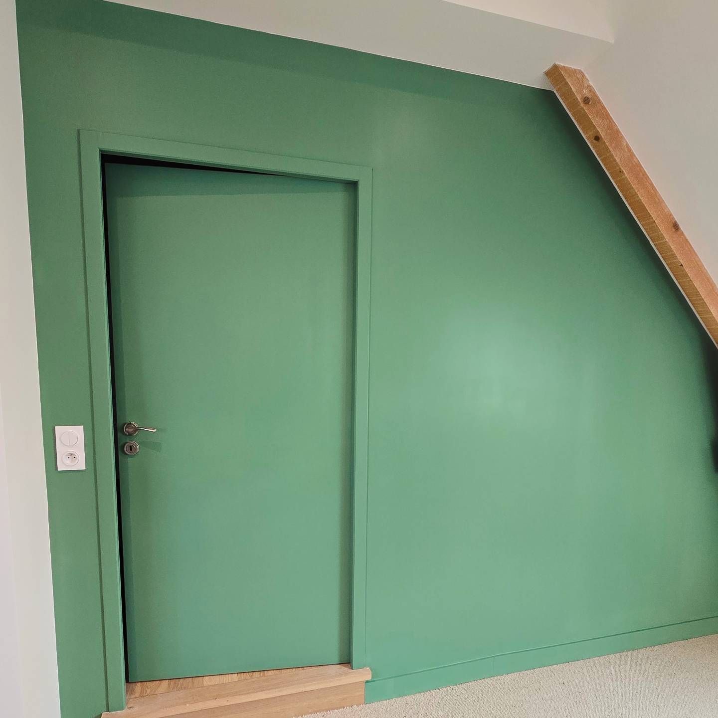 Un mur vert sauge avec une porte assortie et une poutre en bois en diagonale le long du bord incliné du plafond.