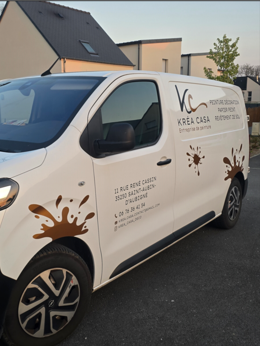 Une camionnette blanche de la société Kréa Casa avec des graphismes à motifs d'éclaboussures de peinture brune, garée à l'extérieur dans une rue.
