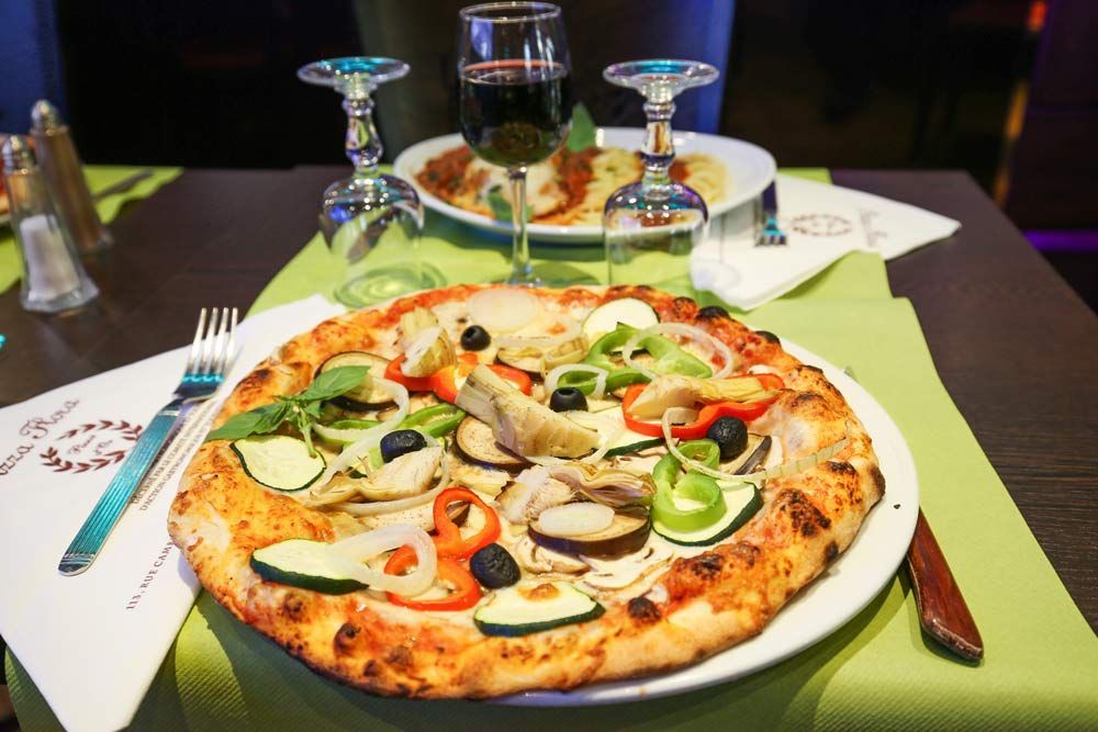 Pizza sur une table avec des sets de table verts, des verres à vin et un verre de vin rouge dans un cadre de restaurant