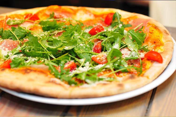 Pizza à la roquette et aux tomates cerises sur une assiette blanche, avec une croûte dorée