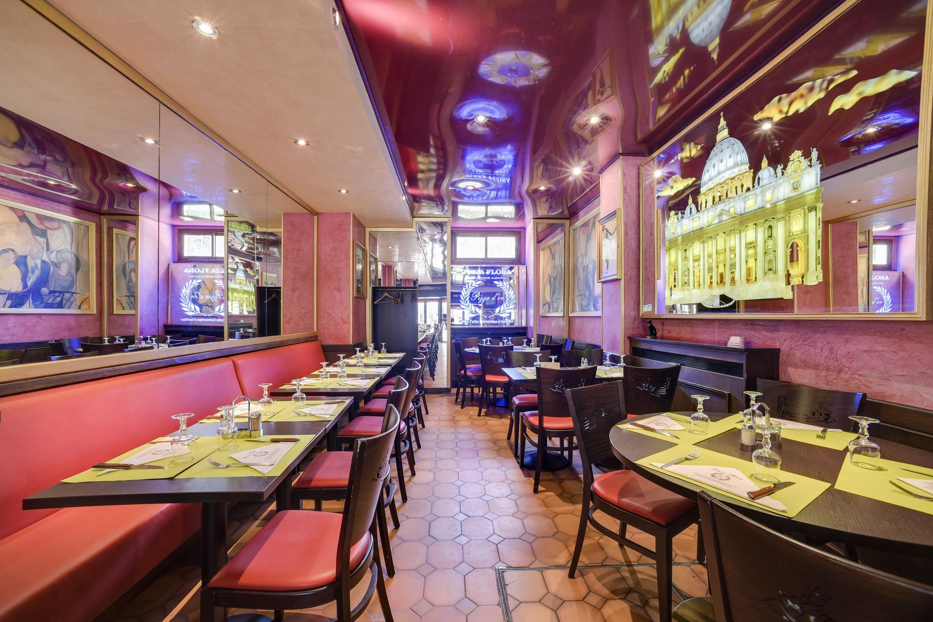 Salle à manger de restaurant vide avec banquettes rouges, tables dressées et murs en miroir sous des lumières colorées au plafond