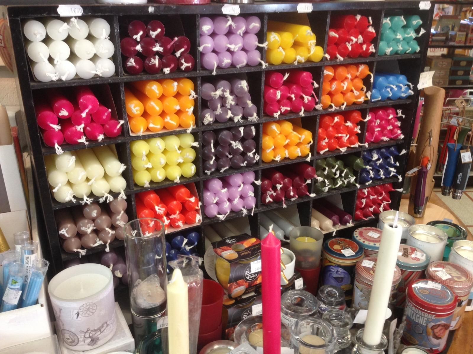 Bougies colorées assorties et pots décoratifs disposés sur des étagères dans une vitrine.