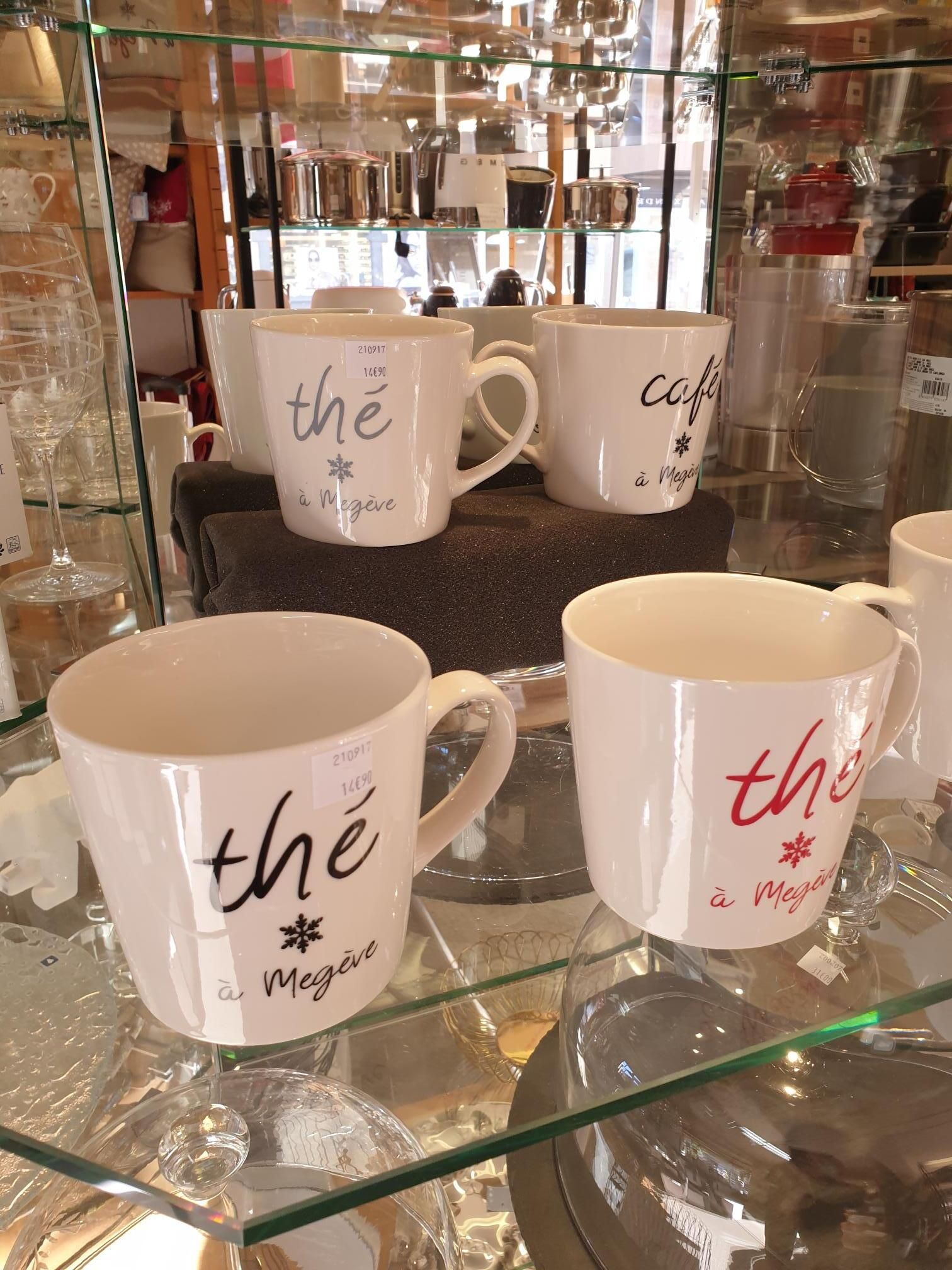 Tasses blanches à motifs floraux présentées sur des étagères en verre dans une vitrine.