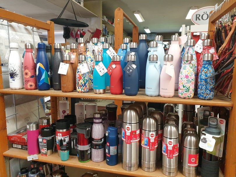 Des étagères garnies de bouteilles d'eau réutilisables et de thermos colorés dans un étalage de magasin.