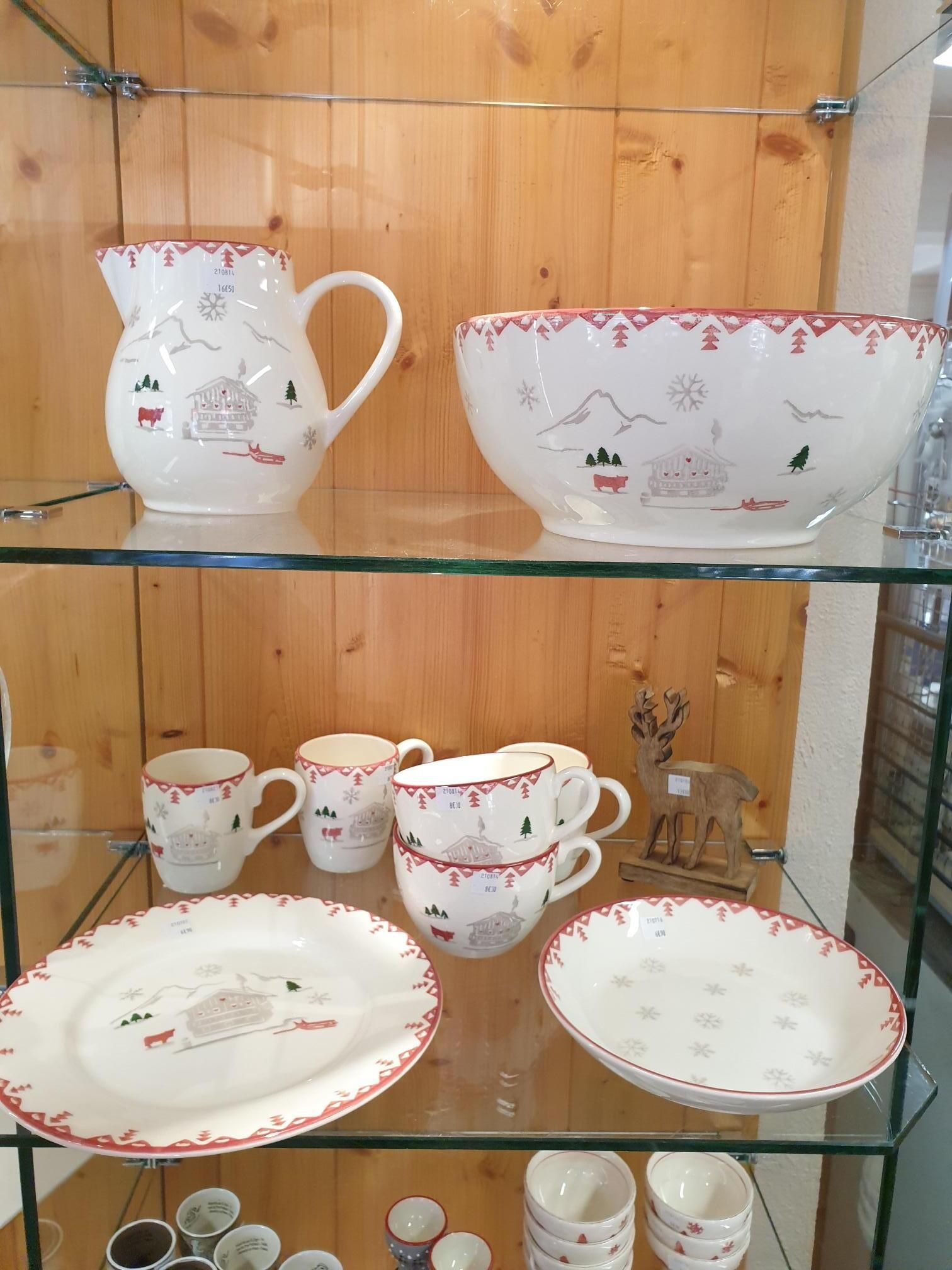 Étagère en verre avec service à thé blanc à motifs floraux : pichet, bol, tasses, soucoupes et assiettes, sur fond de meuble en bois.