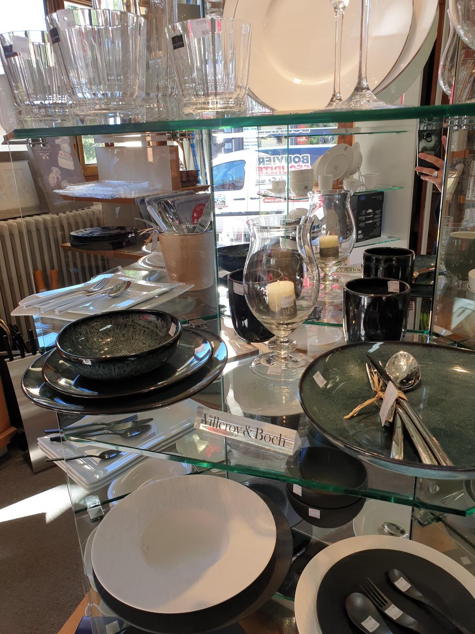 Présentoir de table à fond miroir avec verres, assiettes et couverts empilés, dans un magasin.