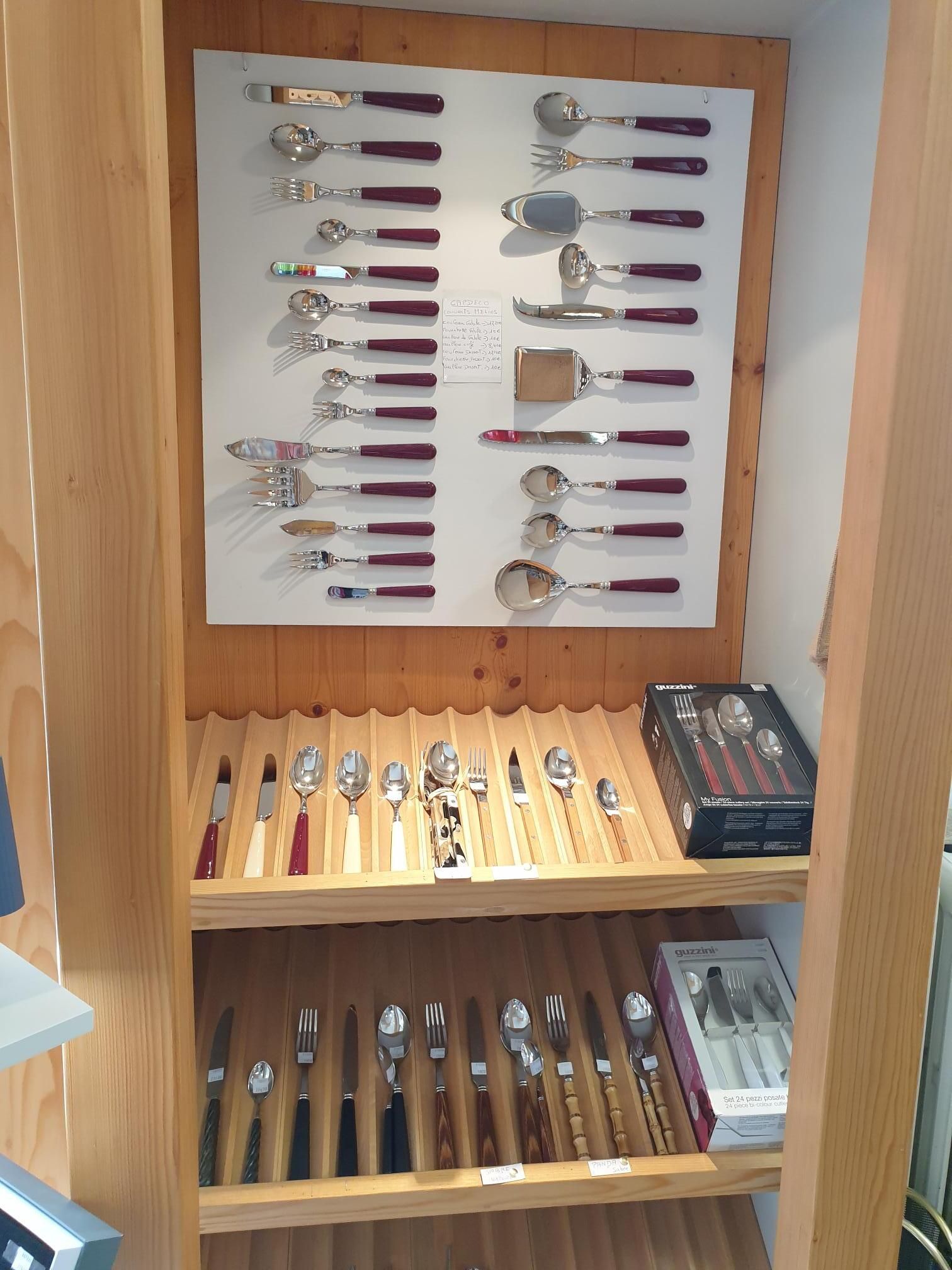 Vitrine en bois remplie de cuillères et d'ustensiles de collection soigneusement rangés sur des étagères.
