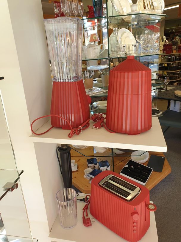 Des appareils de cuisine rouges sont exposés sur une étagère, notamment un mixeur, un grille-pain et un batteur en verre rouge et transparent.