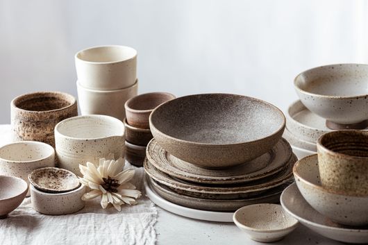 Bols et tasses en céramique aux tons neutres assortis, disposés sur une surface en tissu léger.
