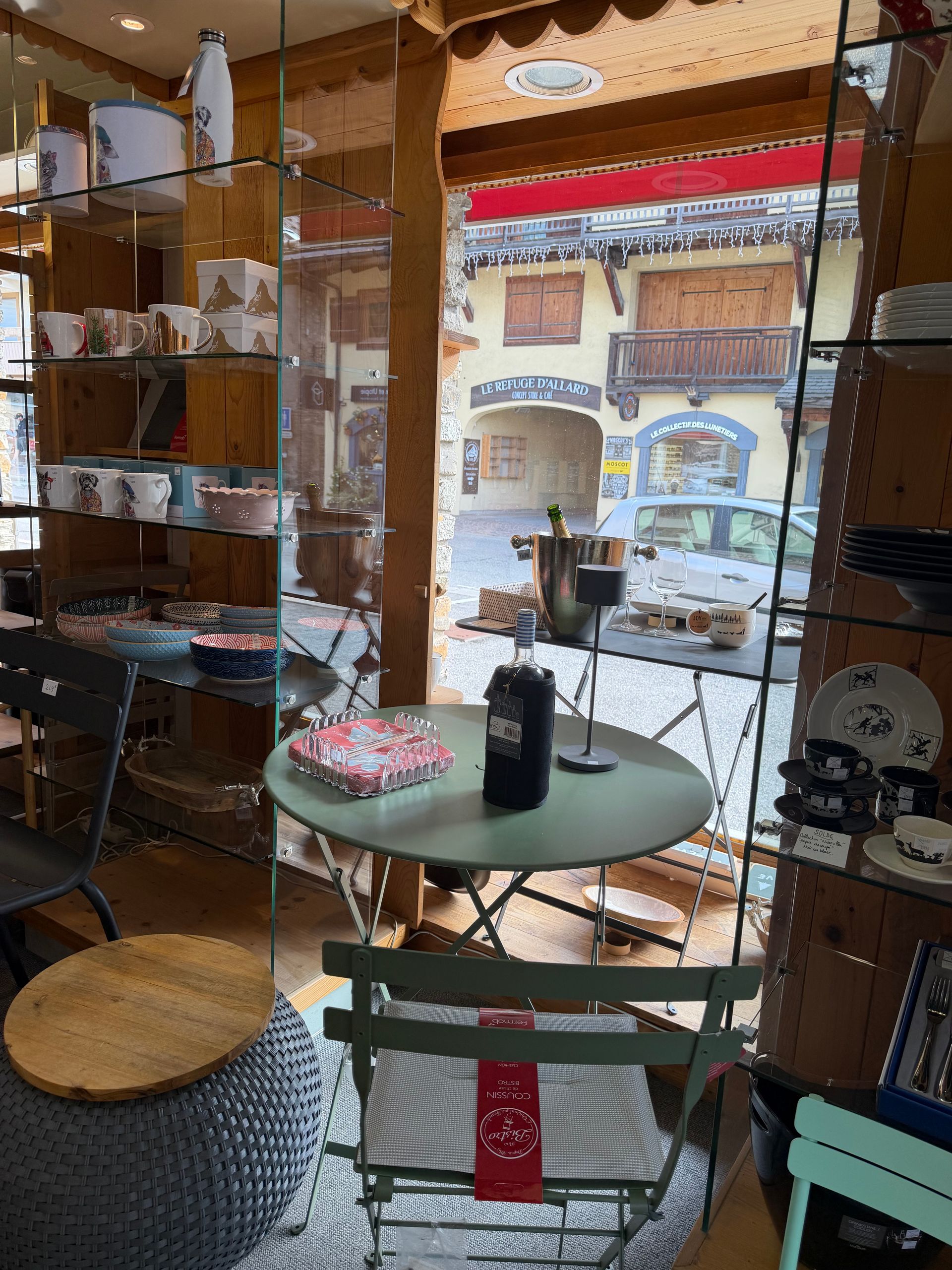 Intérieur d'une boutique avec une petite table ronde, des chaises, des étagères et de lumineuses fenêtres en façade.