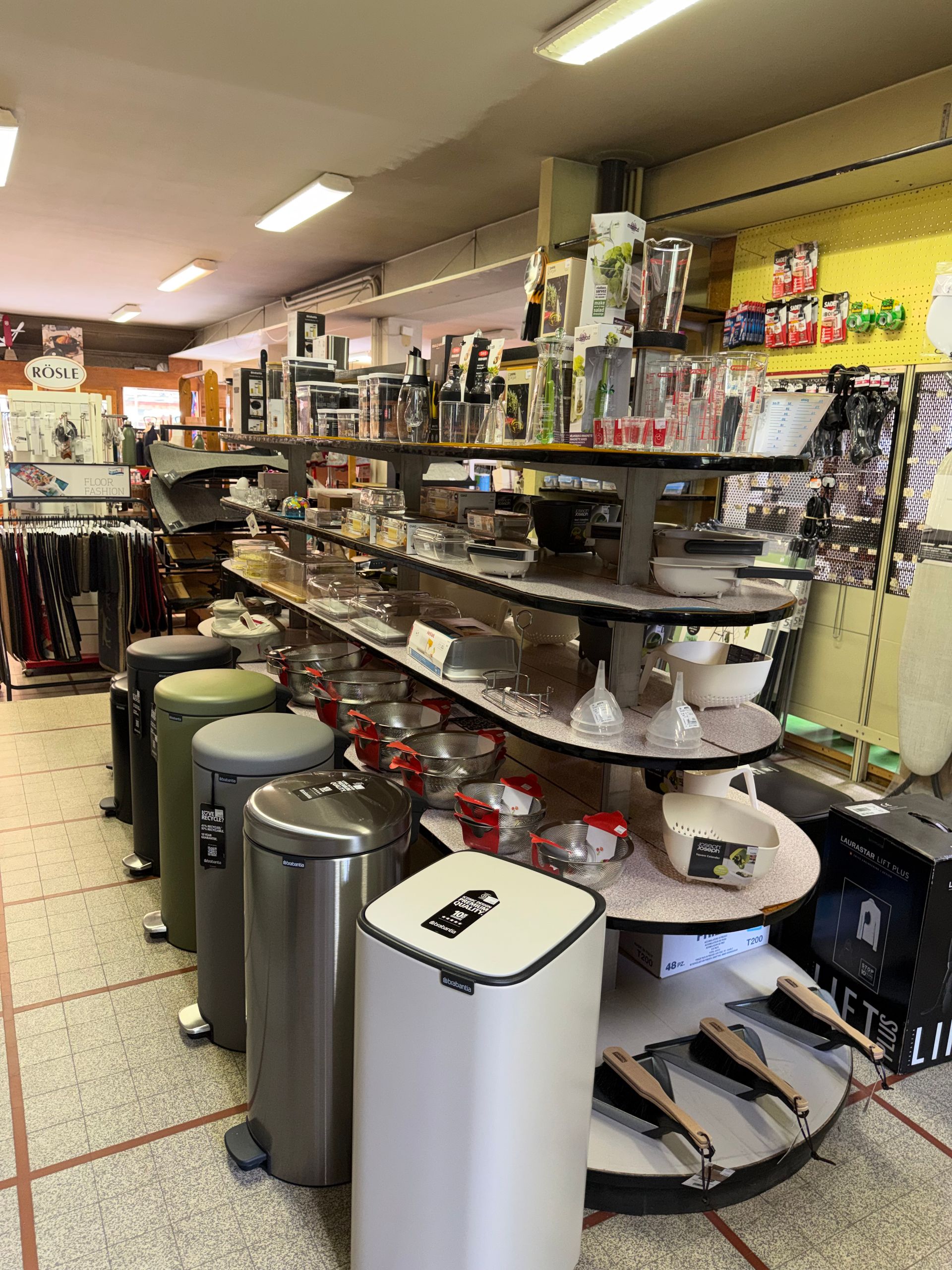 Allée de magasin avec des étagères d'ustensiles de cuisine, d'articles de cuisine et de poubelles métalliques au premier plan.