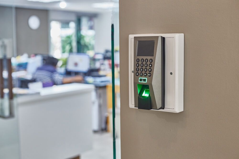Clavier à empreinte digitale fixé au mur vitré d’un bureau, avec un espace de travail flou en arrière-plan