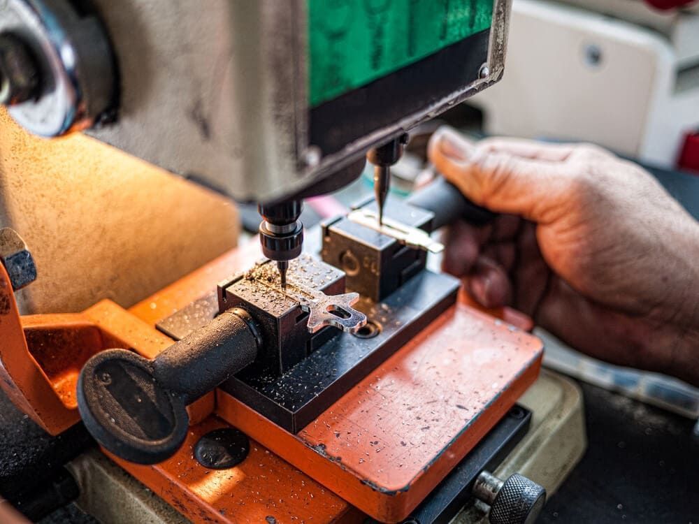 Perçage manuel d’un bloc de métal dans un atelier, avec un socle de machine orange et une main qui le guide