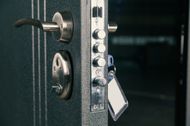 Gros plan d’une porte de coffre-fort avec une poignée métallique et une clé insérée dans la serrure, avec des clés suspendues à proximité
