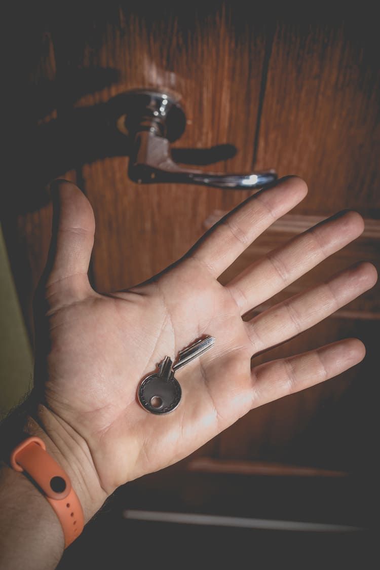 Une main tenant une clé en argent, paume tournée vers le haut, sous un cadenas en métal, sur une surface en bois sombre.