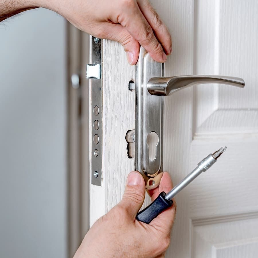 Des mains ajustent une serrure de porte argentée à l’aide d’un tournevis sur une porte blanche