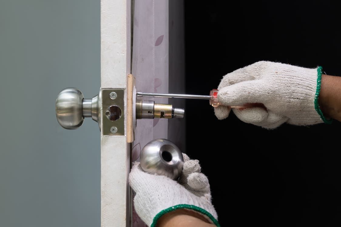 Des mains gantées installent une poignée de porte argentée à l’aide d’un tournevis sur un cadre de porte gris