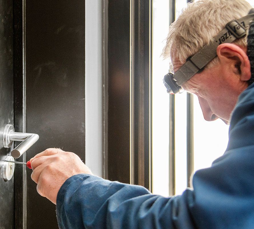 Ouvrier portant une lampe frontale et resserrant une serrure de porte avec un tournevis
