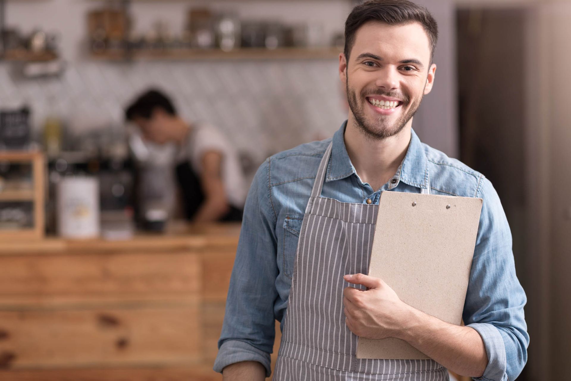 Ein Mann mit Schürze hält in einem Restaurant ein Klemmbrett in der Hand.