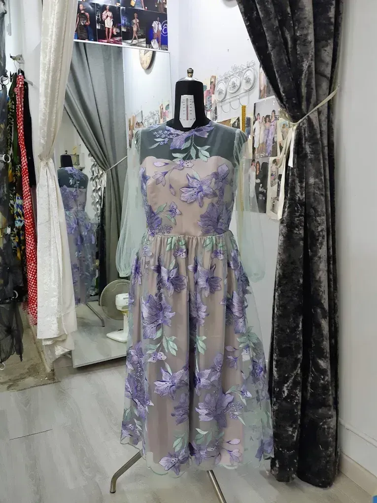 Maniquí de modista que exhibe un vestido hasta la rodilla con bordados florales y mangas transparentes, en un entorno boutique.
