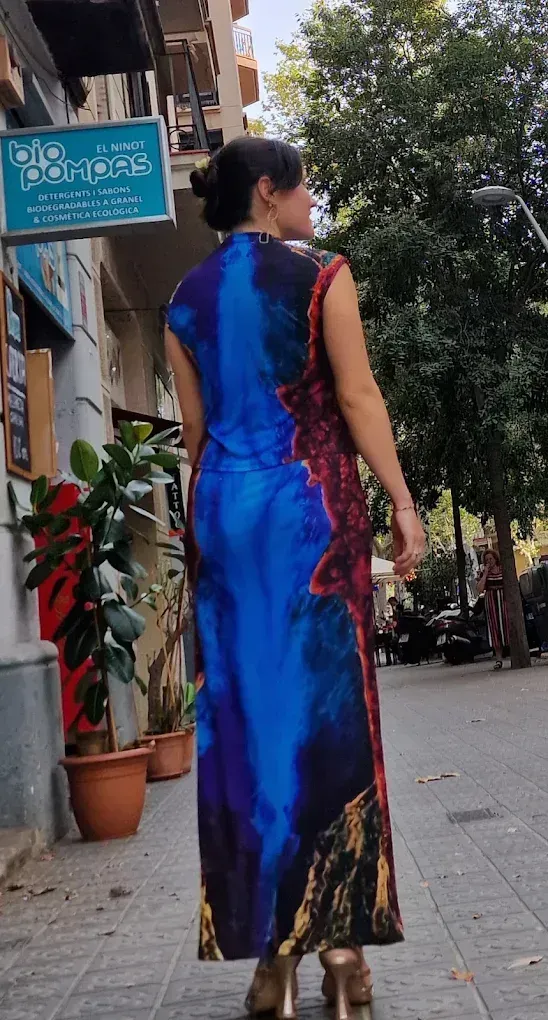 Una mujer con un vestido colorido con estampado abstracto camina por una acera frente a un edificio con un letrero de tienda.