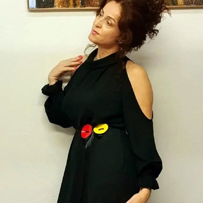 Mujer con vestido negro y cinturón de botones de colores, posando delante de un cuadro.