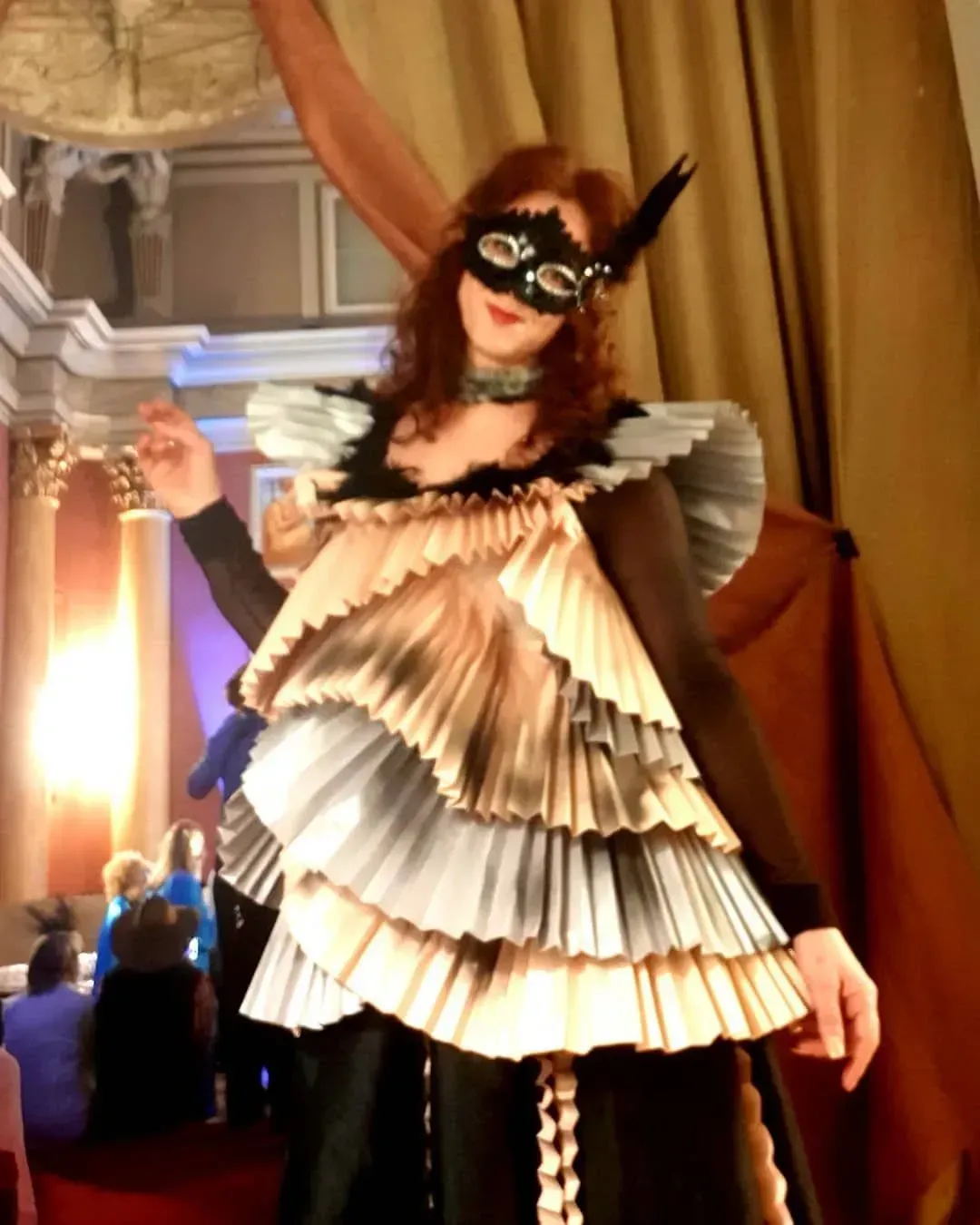 Mujer con vestido plisado escalonado y máscara posa en una pasarela.