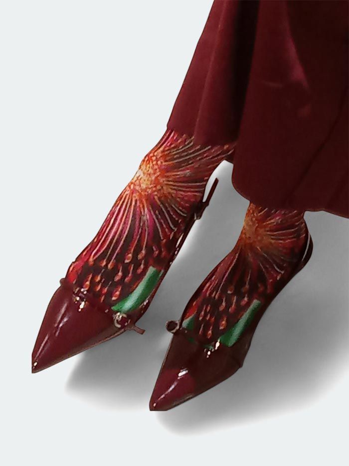 Tacones rojos de punta fina y calcetines estampados a juego, piernas cruzadas.