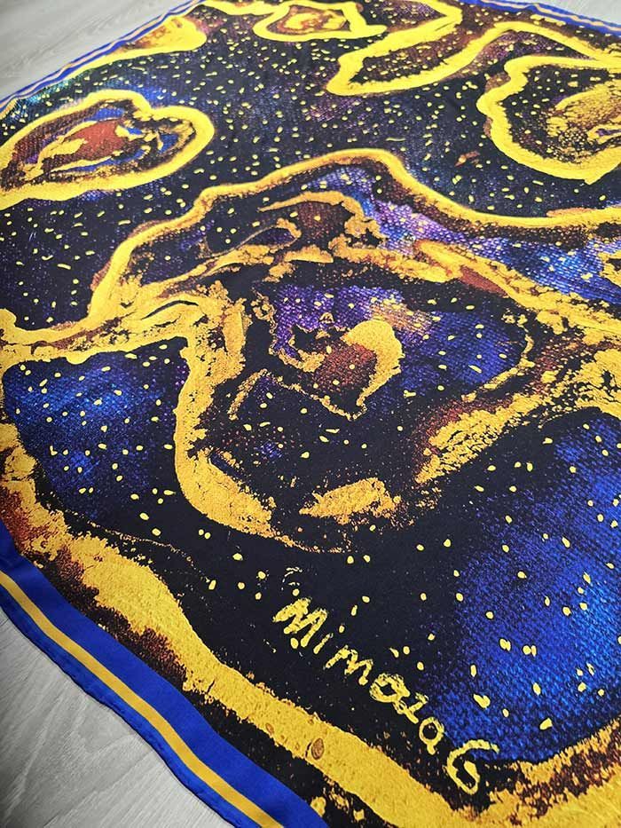 Pañuelo de seda con remolinos amarillos, fondo azul, puntos blancos dispersos y la firma 